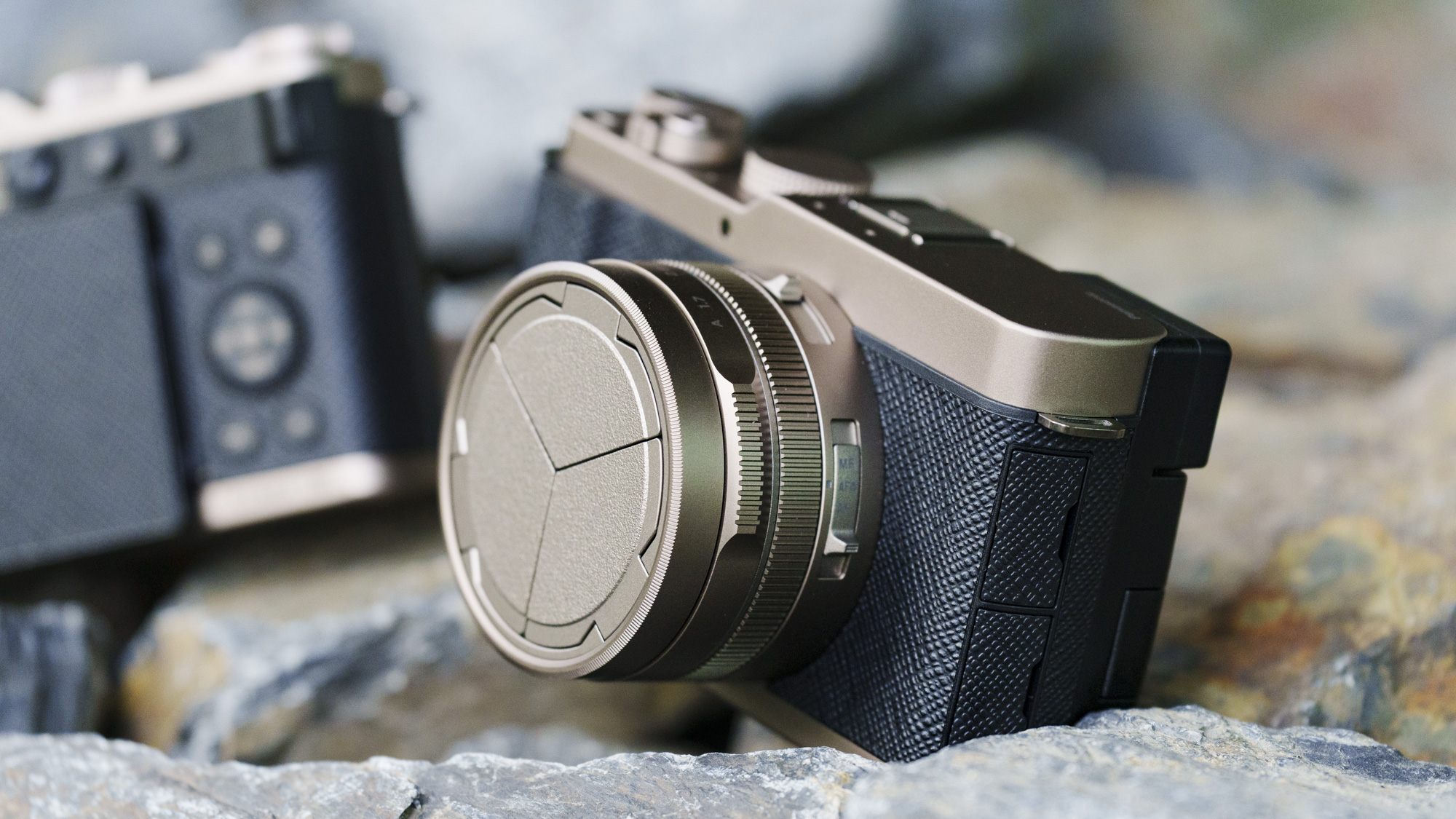 The Gold Titanium Special Edition of the Panasonic Lumix L10 compact camera, sat on gray and rust-colored rocks