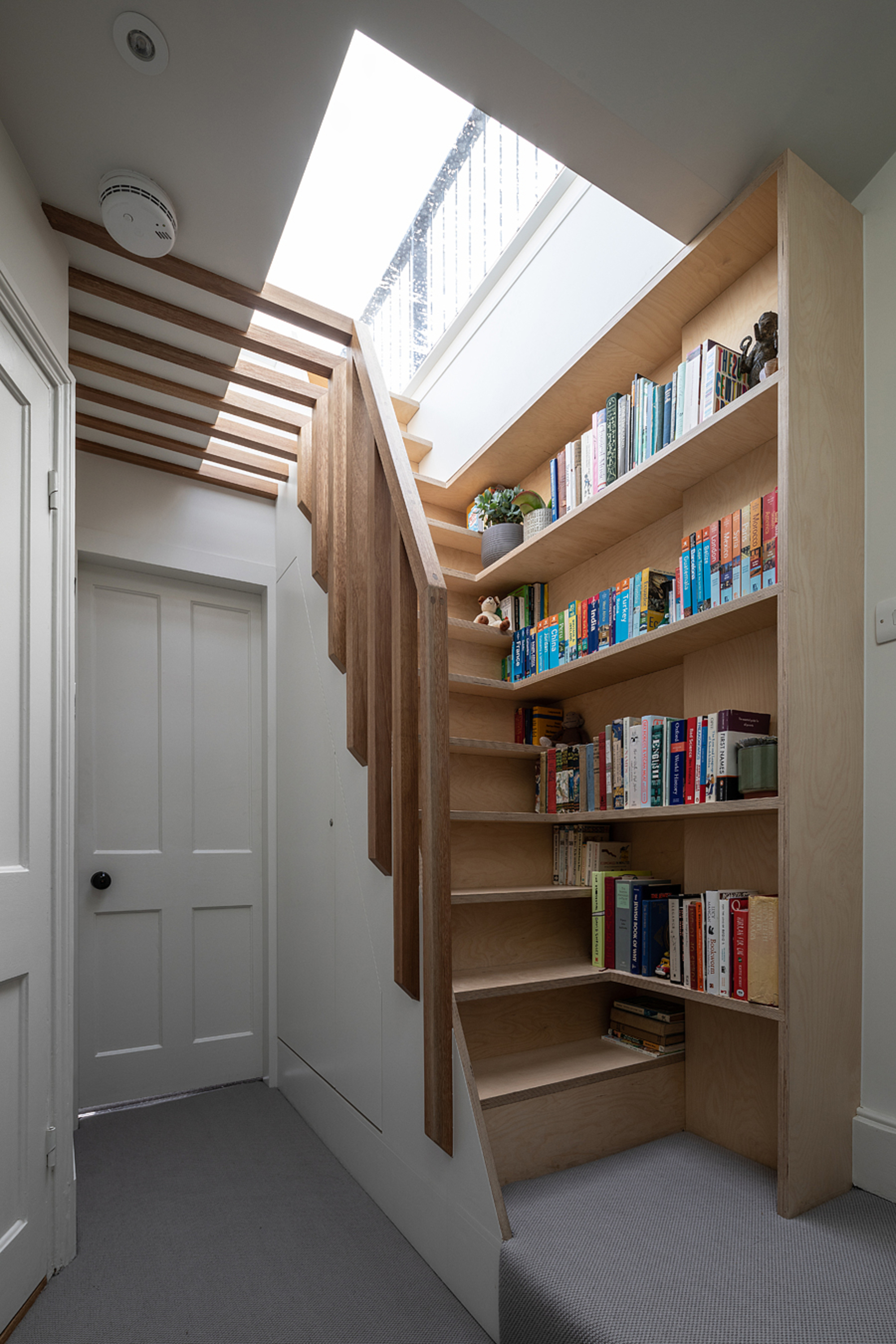 A wooden stairway leading to a loft space with a built-in bookshelf on the side