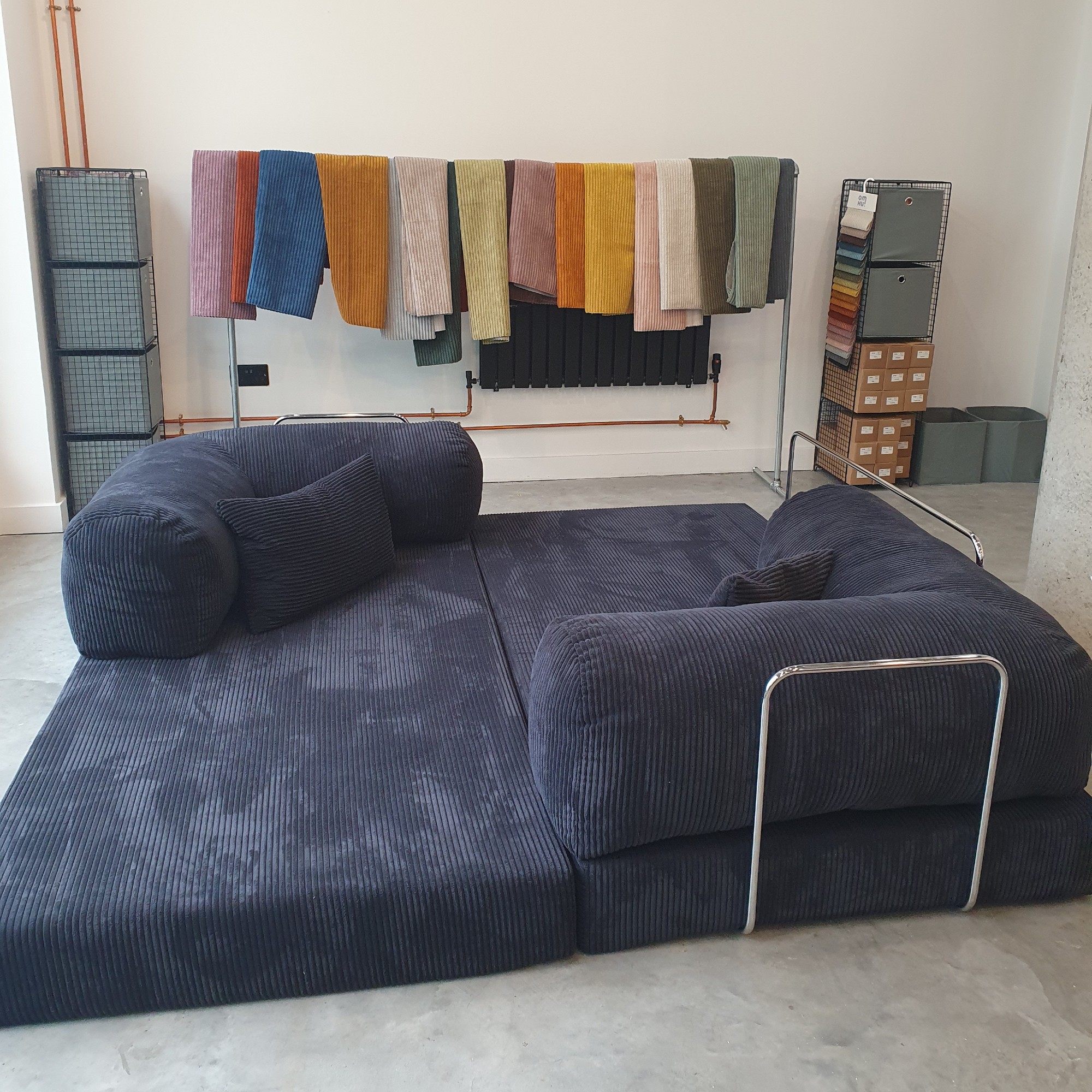 The Teddy sofa by OMHU folded out into the bed arrangement in the brand's London showroom with upholstery samples hung on a rail behind