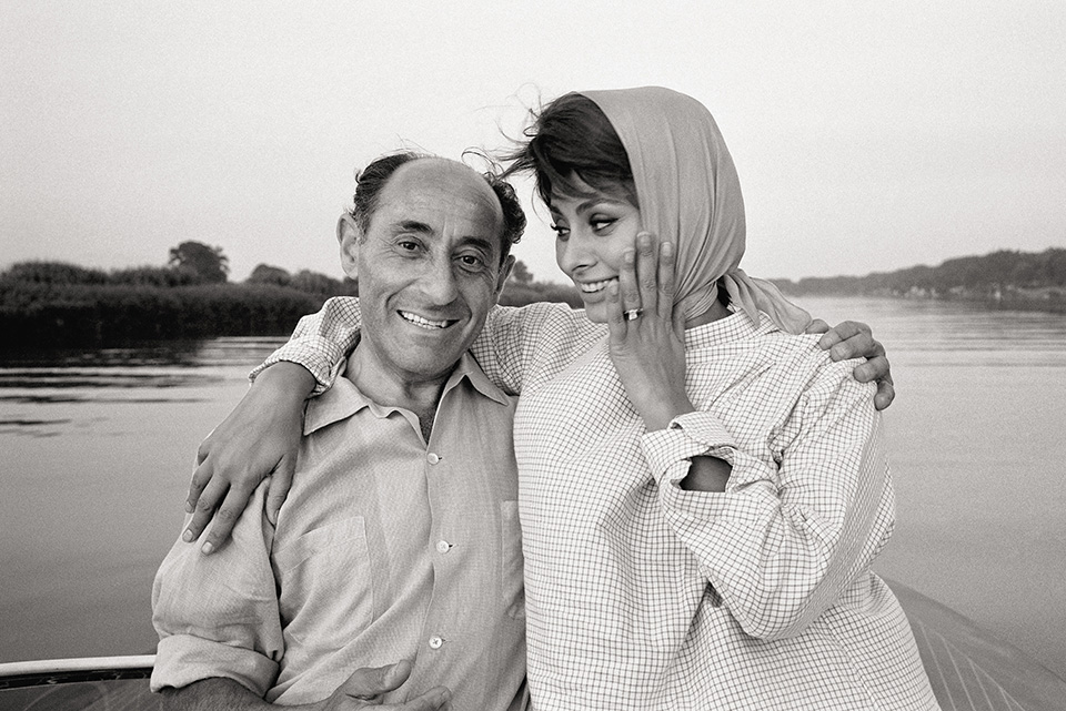 A candid black-and-white photo shows Sophia Loren wearing a headscarf and smiling as she rests her arm around a man&amp;rsquo;s shoulder on a boat.