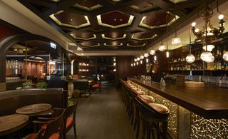 Catalunya, Hong Kong, China. A restaurant with leather seating booths and a long bar counter with high chairs and round pendant lights hanging above it.