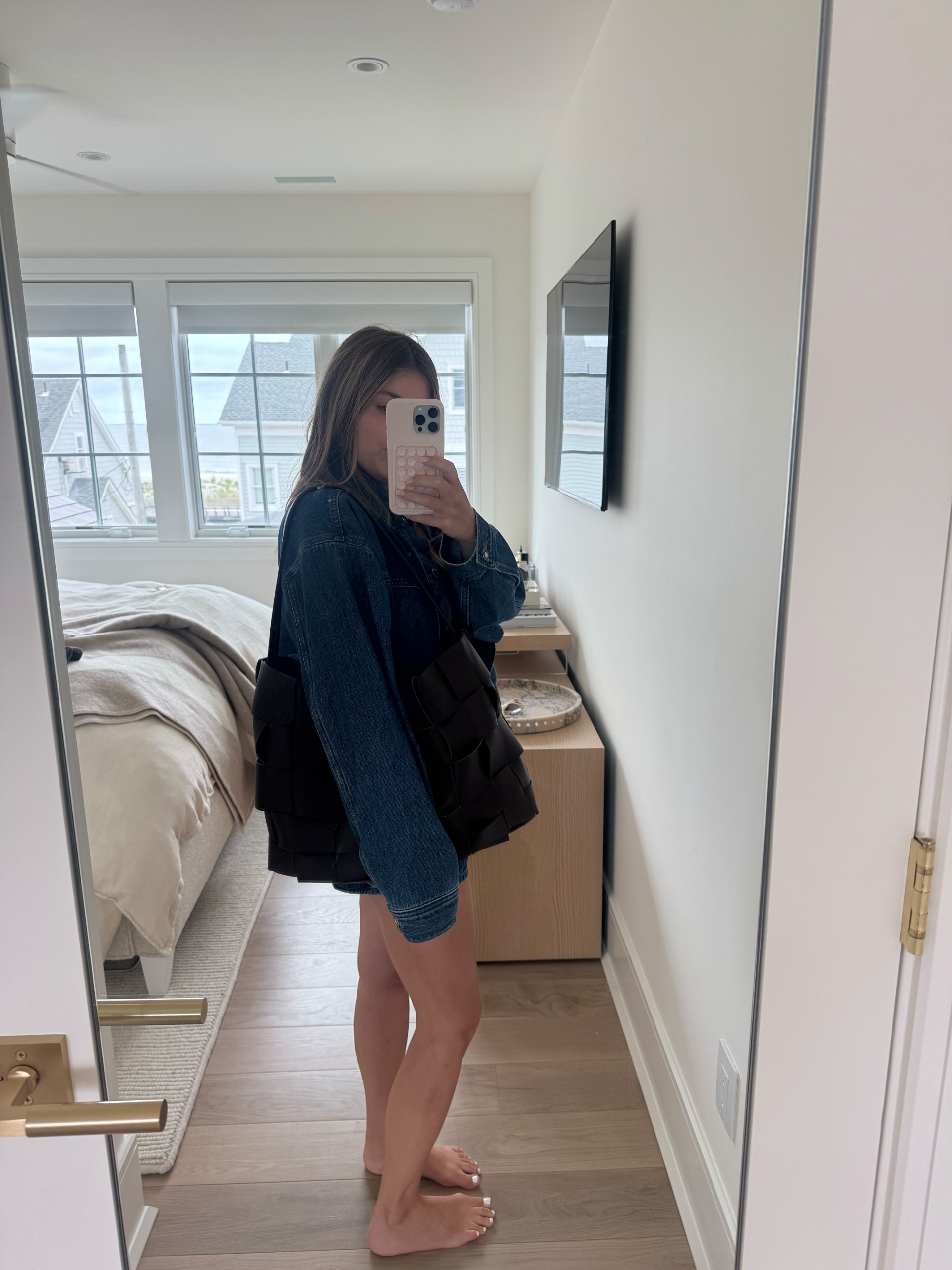Samantha Holender wearing denim taking a mirror selfie carrying woven tote
