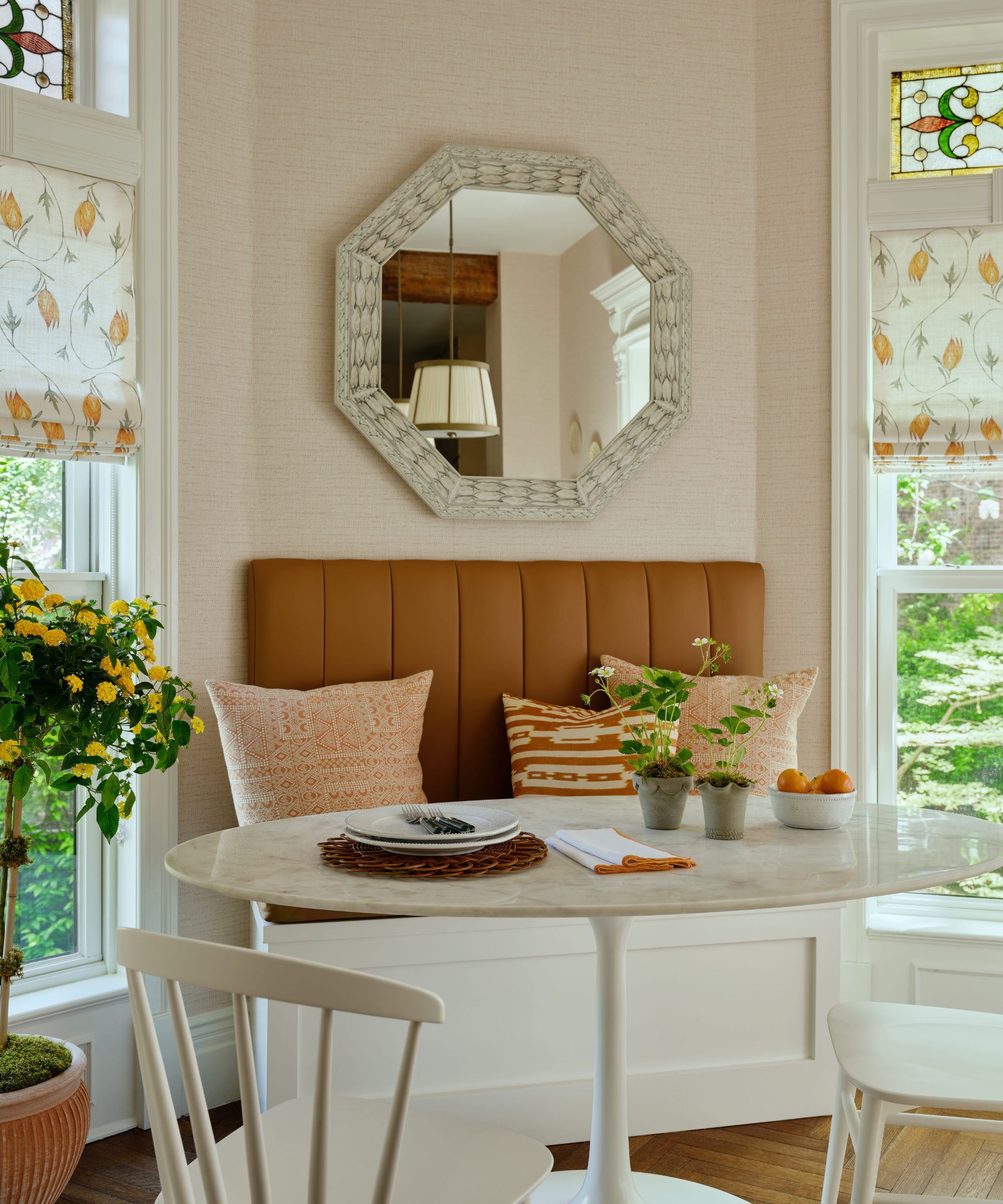 a light neutral kitchen with a small breakfast banquette area with mustard tones and two stained glass windows