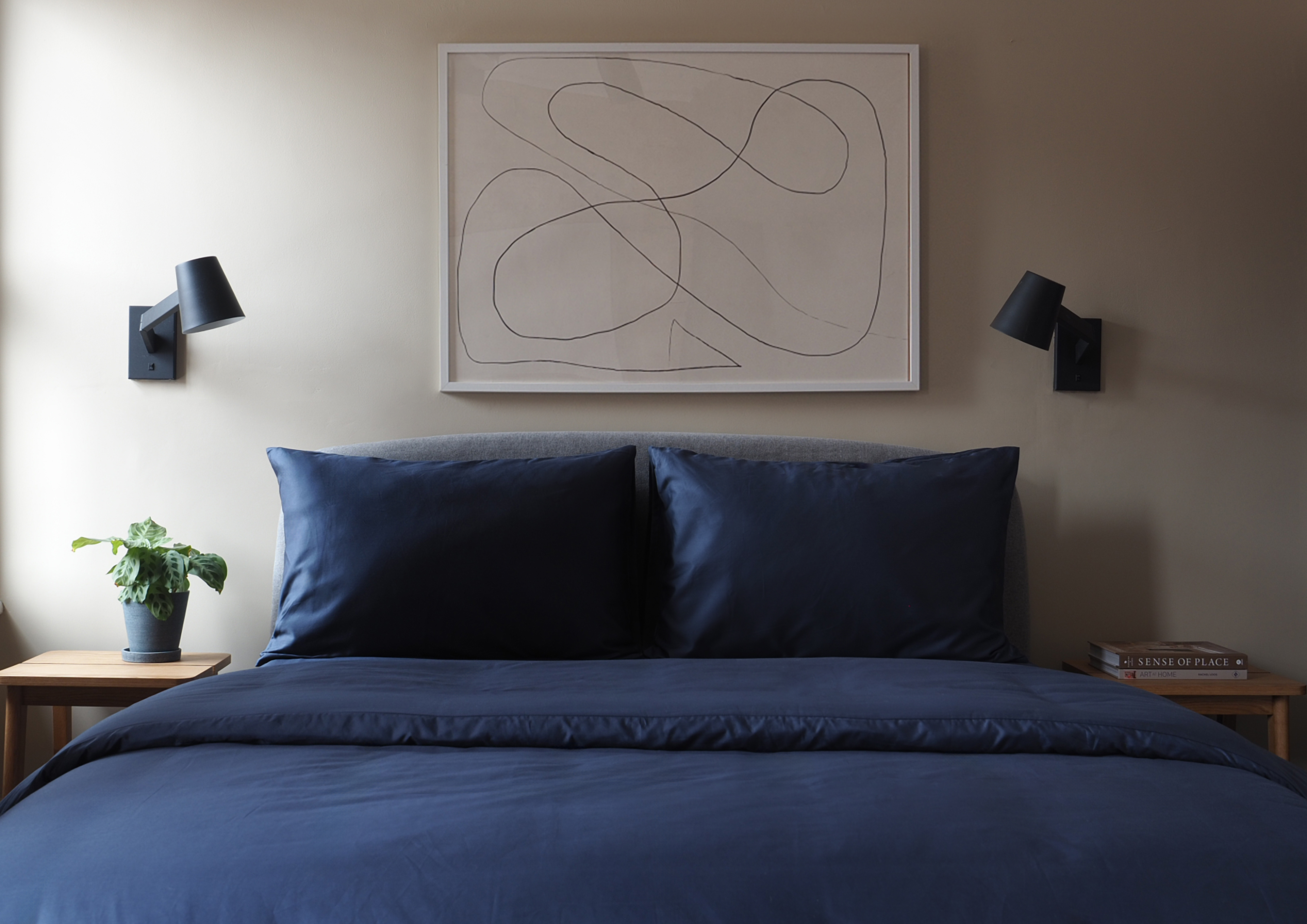 blue bedding in a beige bedroom with art on walls, and black wall lamps