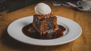 Sticky toffee pudding on a white plate with ice cream on top of it