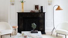 A living room in all white, with a cane standing lamp and a black fireplace