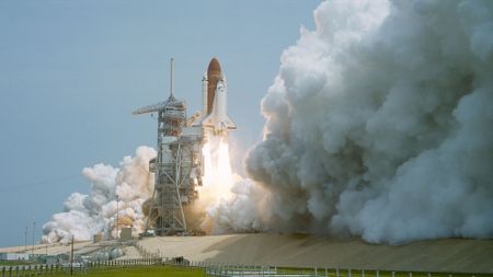 a space shuttle lifts off generating a tremendous plume of steam
