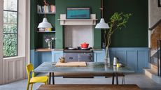 Green and blue kitchen with dining table and gray aga inside a range