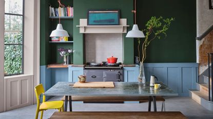 Green and blue kitchen with dining table and gray aga inside a range