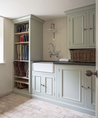 Mudroom inspired laundry room ideas with a floor-to-ceiling shelving unit filled with boots and pale gray painted cabinetry.