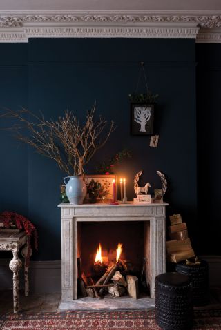 a lit fireplace within a dark blue living room, with festive accessories, and a multi-colored rug on the floor