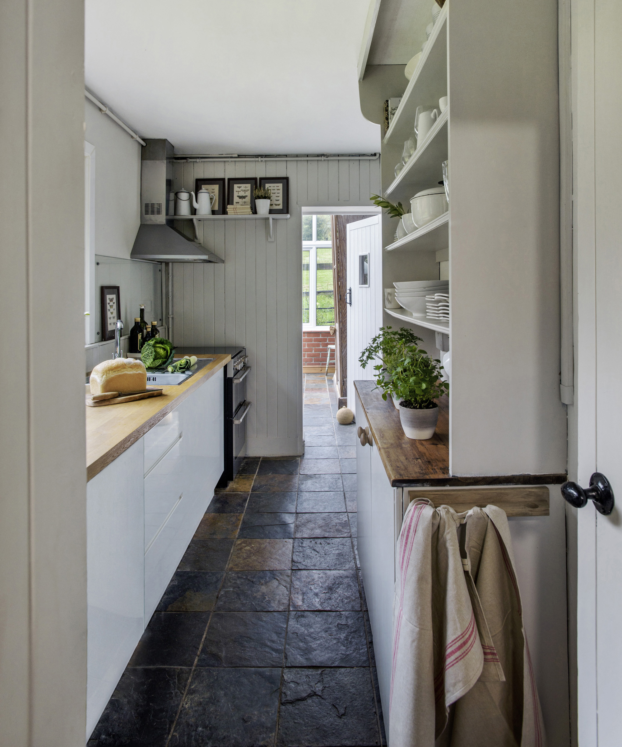 A galley kitchen with farmhouse style cabinets and textured natural stone floors