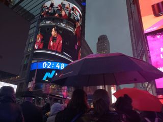 At 4 Times Square on Nov. 26, 2018, women huddle under an umbrella to watch NASA TV footage of the InSight Mars landing.