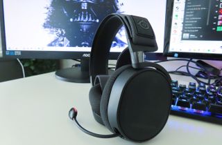 Bästa gaming-headset: Ett par svarta SteelSeries Arctis 7+ står på ett vitt skrivbord med en gaming setup i bakgrunden.