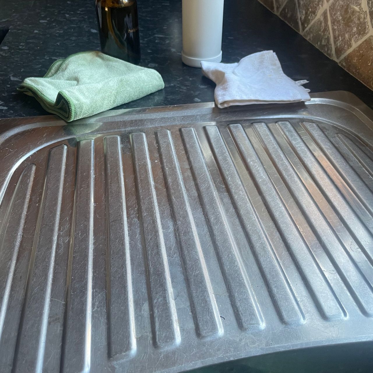 Clean draining board with cleaning products and cloths next to it