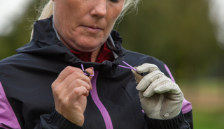 A golfer adjusts the toggles on the adidas Women's Rain.RDY Golf Jacket