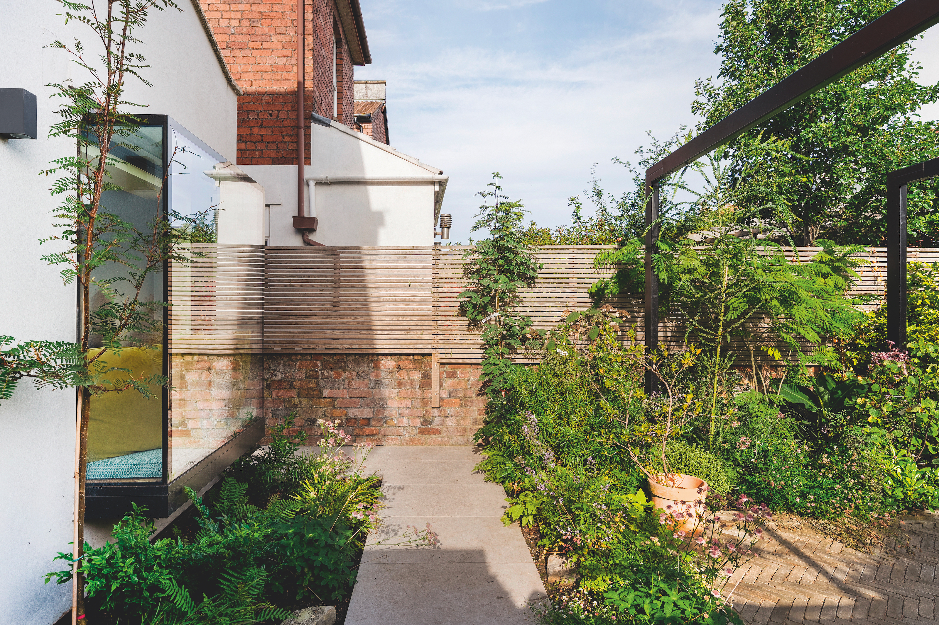 Garden space with glass viewing box looking out onto the exterior, and a black pergola covered in greenery.