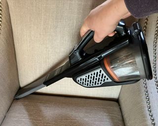 Black + Decker dustbuster handheld vacuum with built-in crevice tool being used to clean upholstered furniture