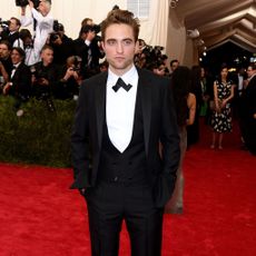 Robert Pattinson stands with hands in pockets on the red carpet.