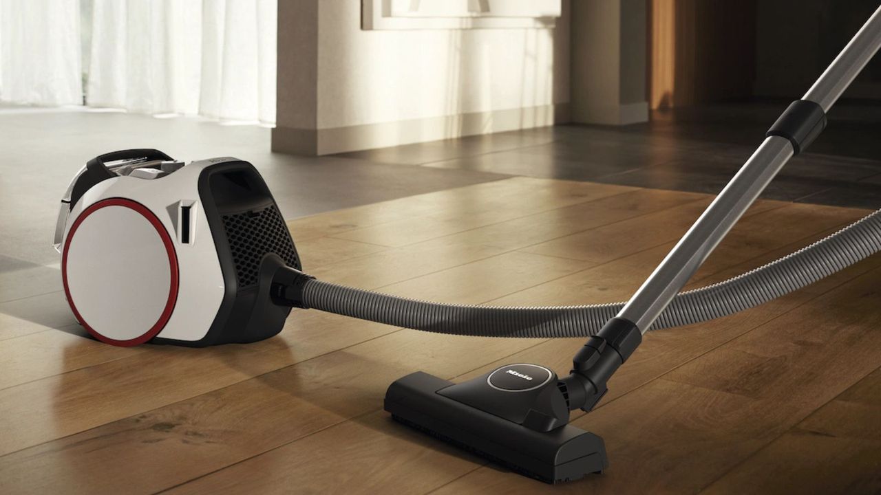 Miele Boost CX1 canister vacuum cleaner on wooden floor with white curtains in background