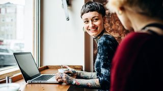 A smiling woman uses one of the best laptops for battery life in a cafe