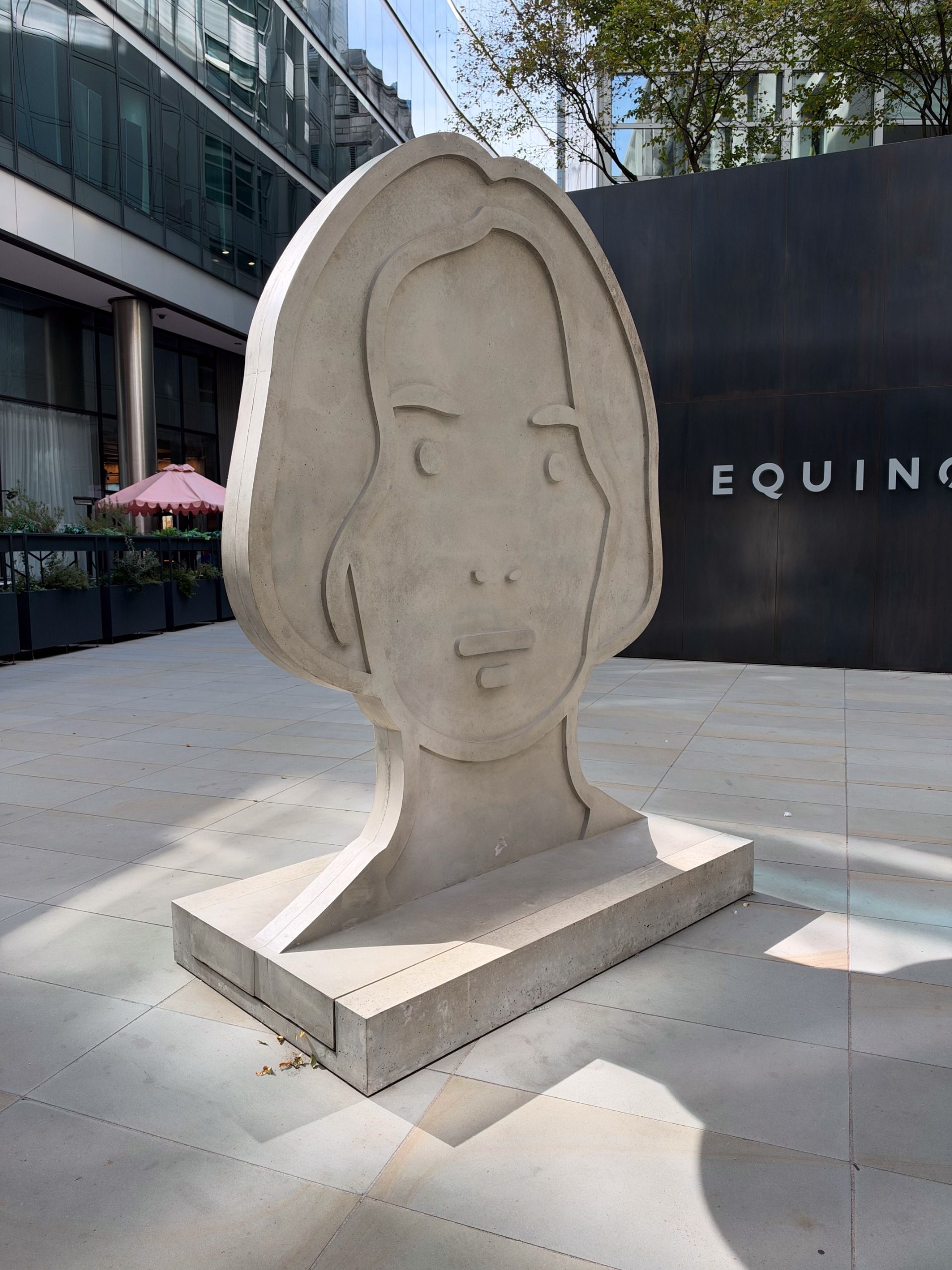 Front view of a large minimalist concrete face sculpture displayed outside a modern glass building.