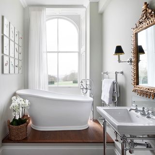 Small white slipper bath in bathroom with raised wooden platform and smart heritage taps