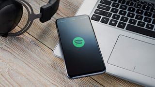 spotify on a phone next to a laptop and a pair of headphones
