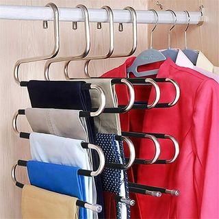 4 s shaped metal clothes hangers with folded trousers handing from each rung hanging in a wooden closet