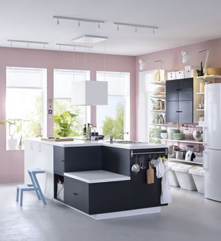 Black kitchen island in a white kitchen with bifold doors and pink walls