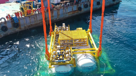 A submersible data center pod is lowered underwater via crane. 
