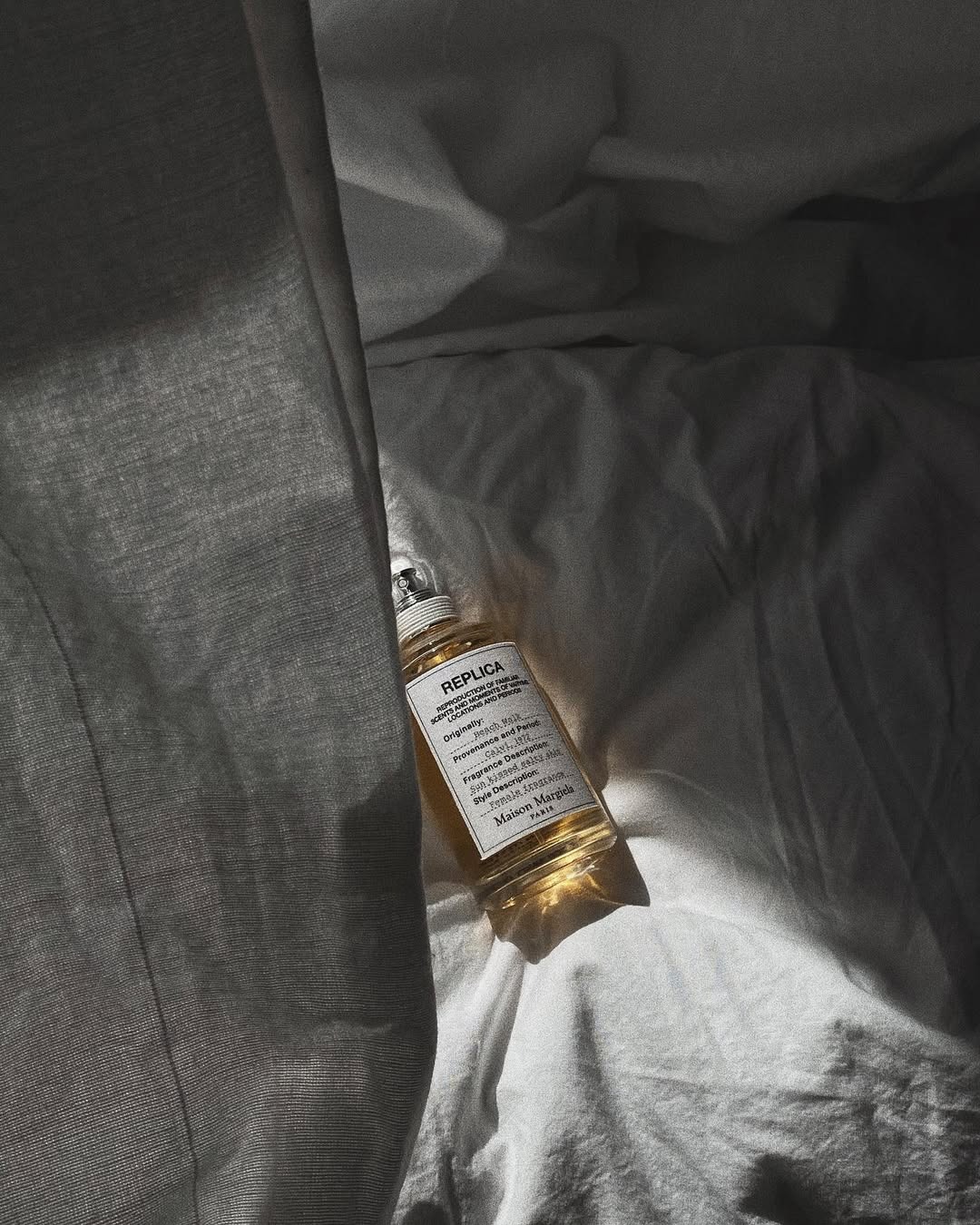 An image of a Maison Margiela Replica fragrance lying on linen sheets.