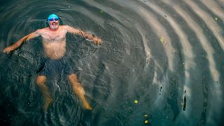 Man swimming outdoors wearing bright blue swim cap
