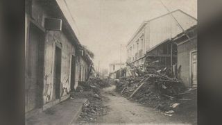 A black and white photograph showing the damage caused by the Vallenar earthquake in Chile (1922). We see the view of a street, with damaged buildings either side and lots of rubble to the side.