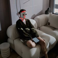 Woman sitting on a couch while wearing an LED face mask.