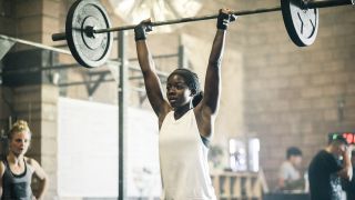 Woman performs overhead press exercise with barbell