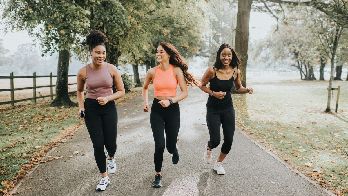 Three women running outside along a park track laughing