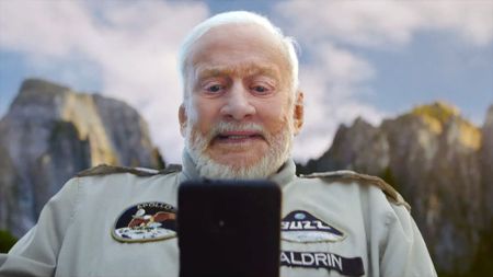 a white-haired man looks down at his phone backdropped by mountains