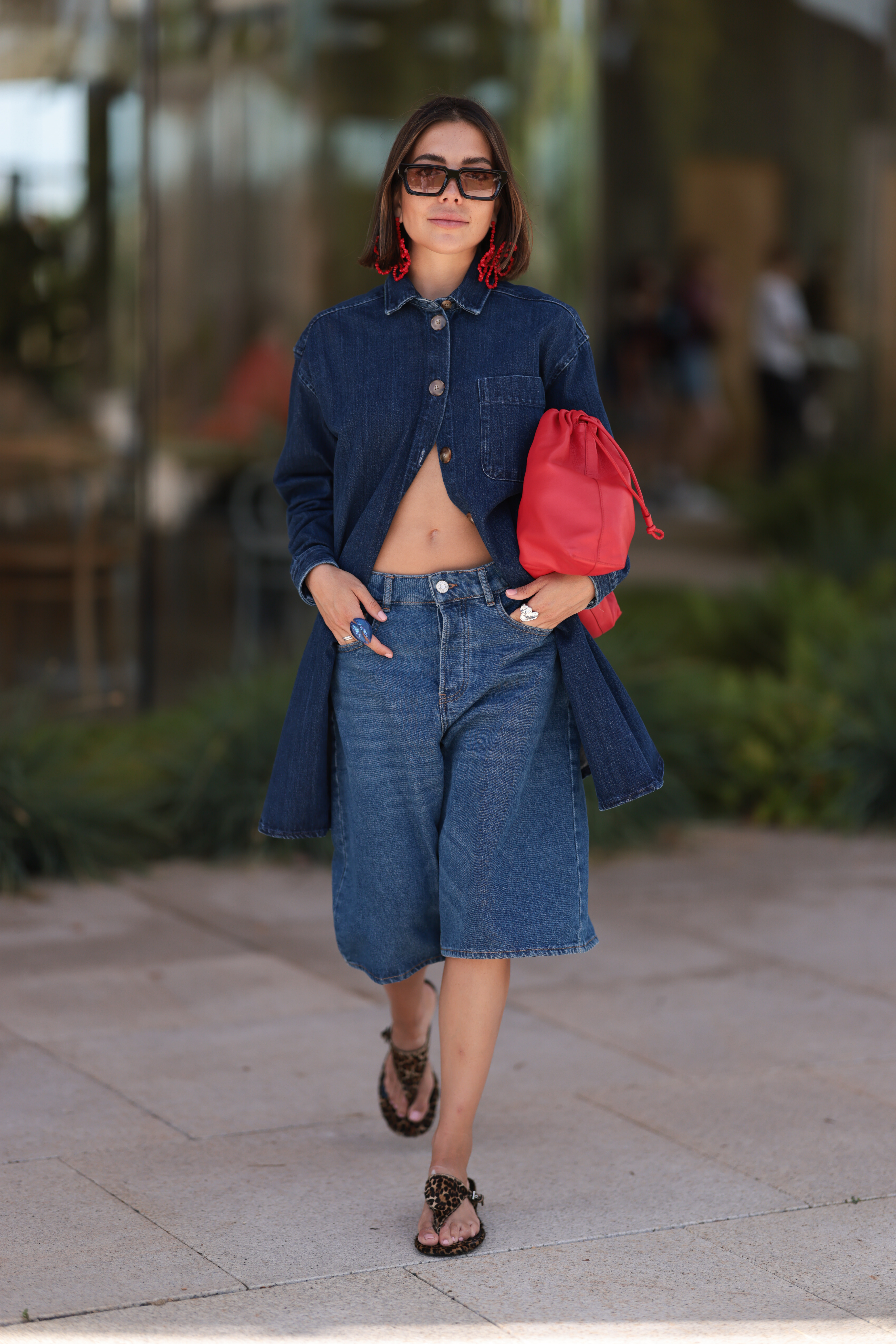 woman wearing blue denim top, denim bermuda shorts, red bag, black sandals