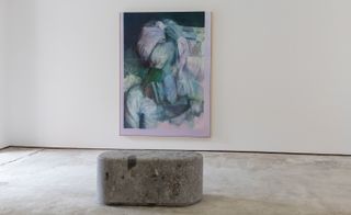 Abstract painting on a white wall in a gallery, with a grey carved stone bench in the center of the room