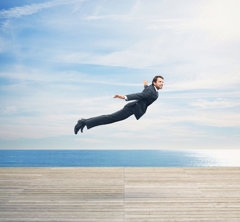 A man in a business suit flies over a boardwalk.