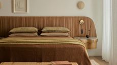 a bed with a ruched leather headboard and neutral bed sheets with a built in marble topped side table