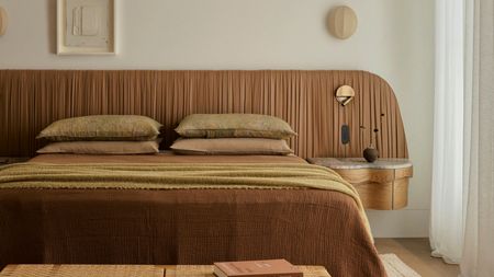 a bed with a ruched leather headboard and neutral bed sheets with a built in marble topped side table
