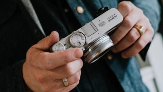 Hands holding Fujifilm X100V camera in use, showing top plate dials
