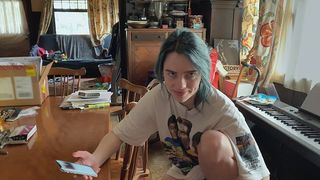 Billie Eilish grinning at the camera in a casual outfit at home