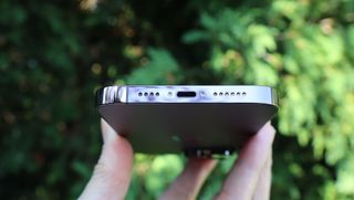En hand som håller upp en Apple iPhone 14 Pro Max utomhus, med undersidan riktad mot kameran.