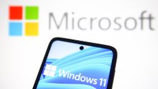 A phone showing the Windows 11 logo, with the Microsoft logo shown on a white background behind.
