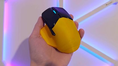 Hand holding HyperX Pulsefire Saga Pro mouse yellow shell in front.