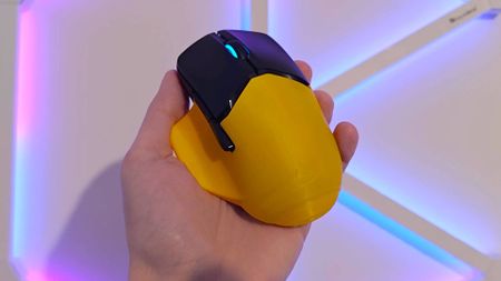 Hand holding HyperX Pulsefire Saga Pro mouse yellow shell in front.