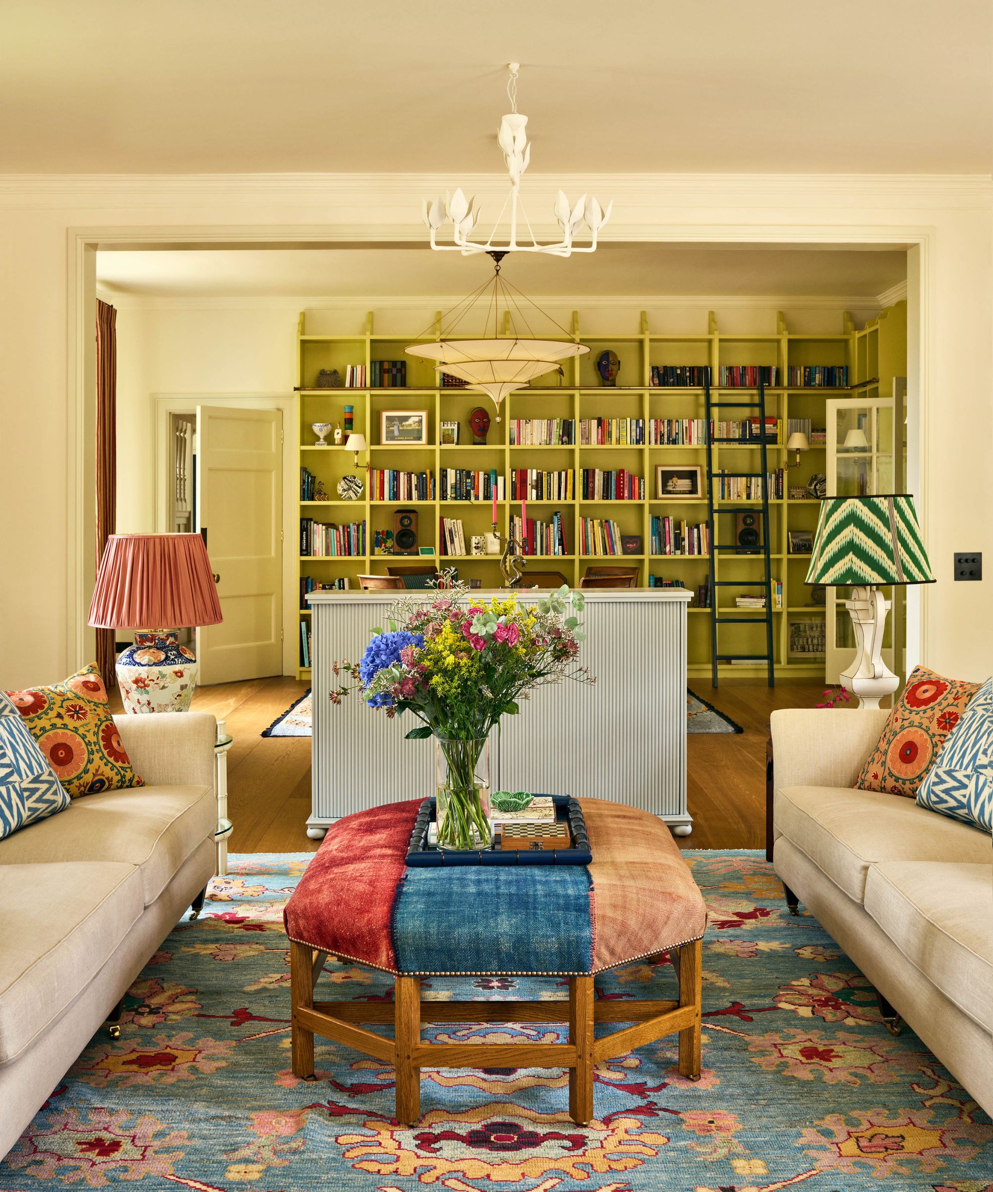Living room with lime green painted built-in bookshelves, a floral rug, a colourful ottoman on top, a TV cabinet, and two beige sofas with floral pillows
